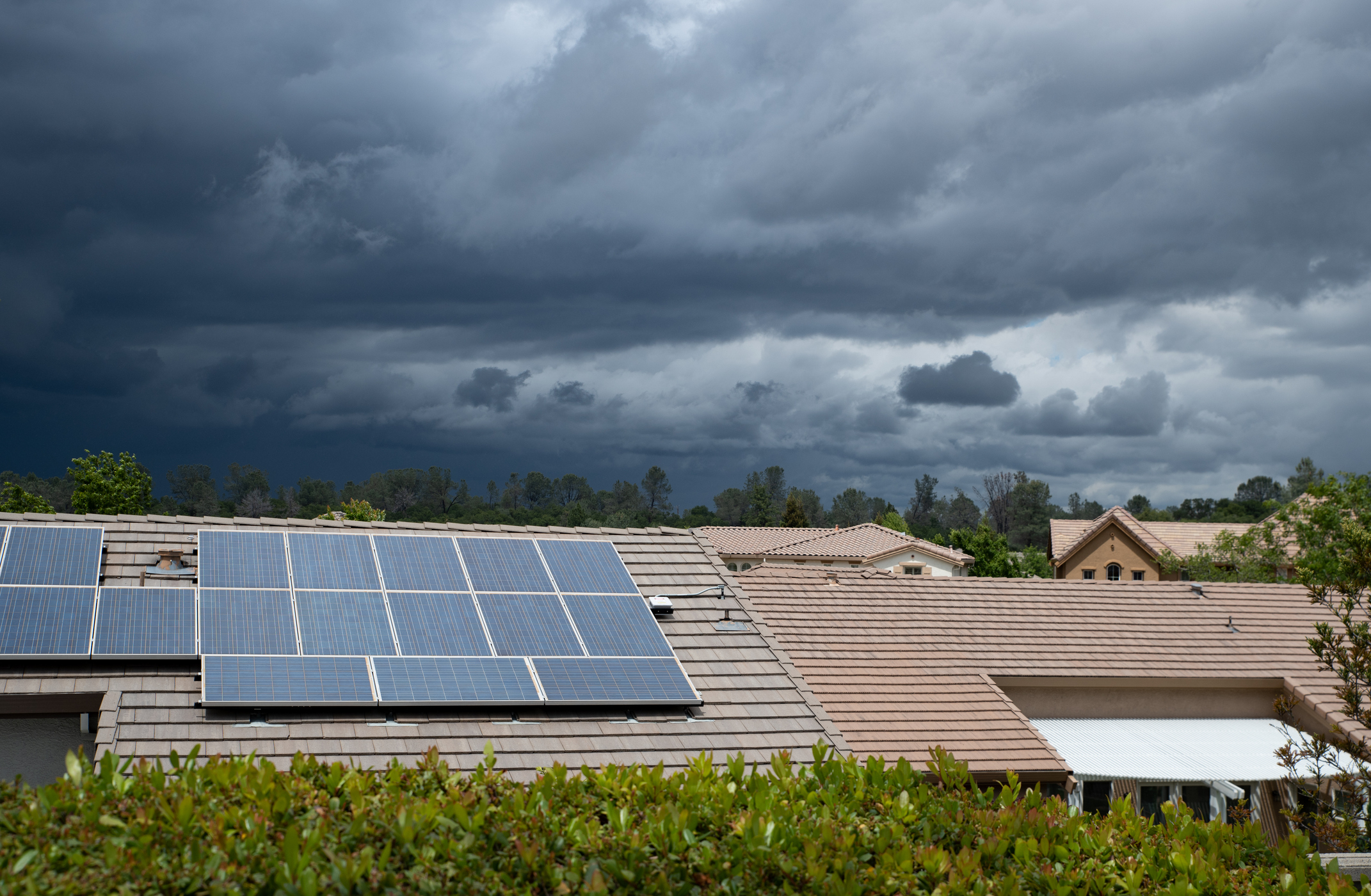 Rooftop solar panels on suburban homes under dark, stormy skies with dense clouds.